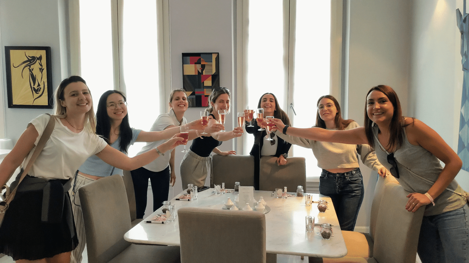 Un groupe de femmes souriantes levant leurs verres pour un toast lors d'un atelier de célébration d'enterrement de vie de jeune fille (EVJF). L'atmosphère est joyeuse et détendue.