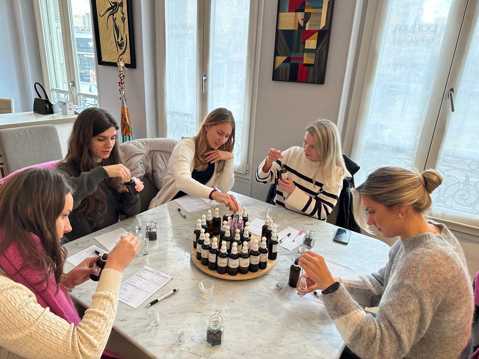 Participants en atelier de création de parfum mélangeant différentes essences et matières premières autour d’une table pour composer leur propre fragrance.